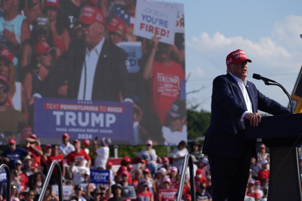 Trump speaks at the campaign rally in Butler on July 13. He's standing behind a lectern while wearing a red baseball cap that says: "Make America Great Again." A live video of him speaking appears on a large screen behind him.