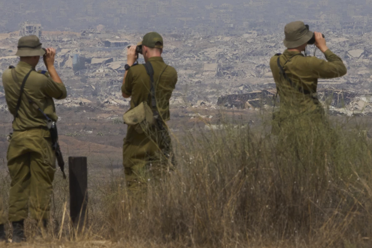 Israeli soldiers uses binoculars to look at damaged buildings in the Gaza Strip, from southern Israel, Wednesday, Aug. 13, 2025.