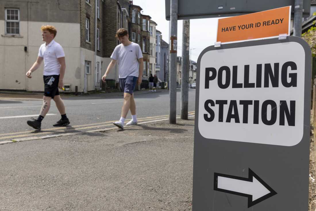 People walk past a sign for a polling station.