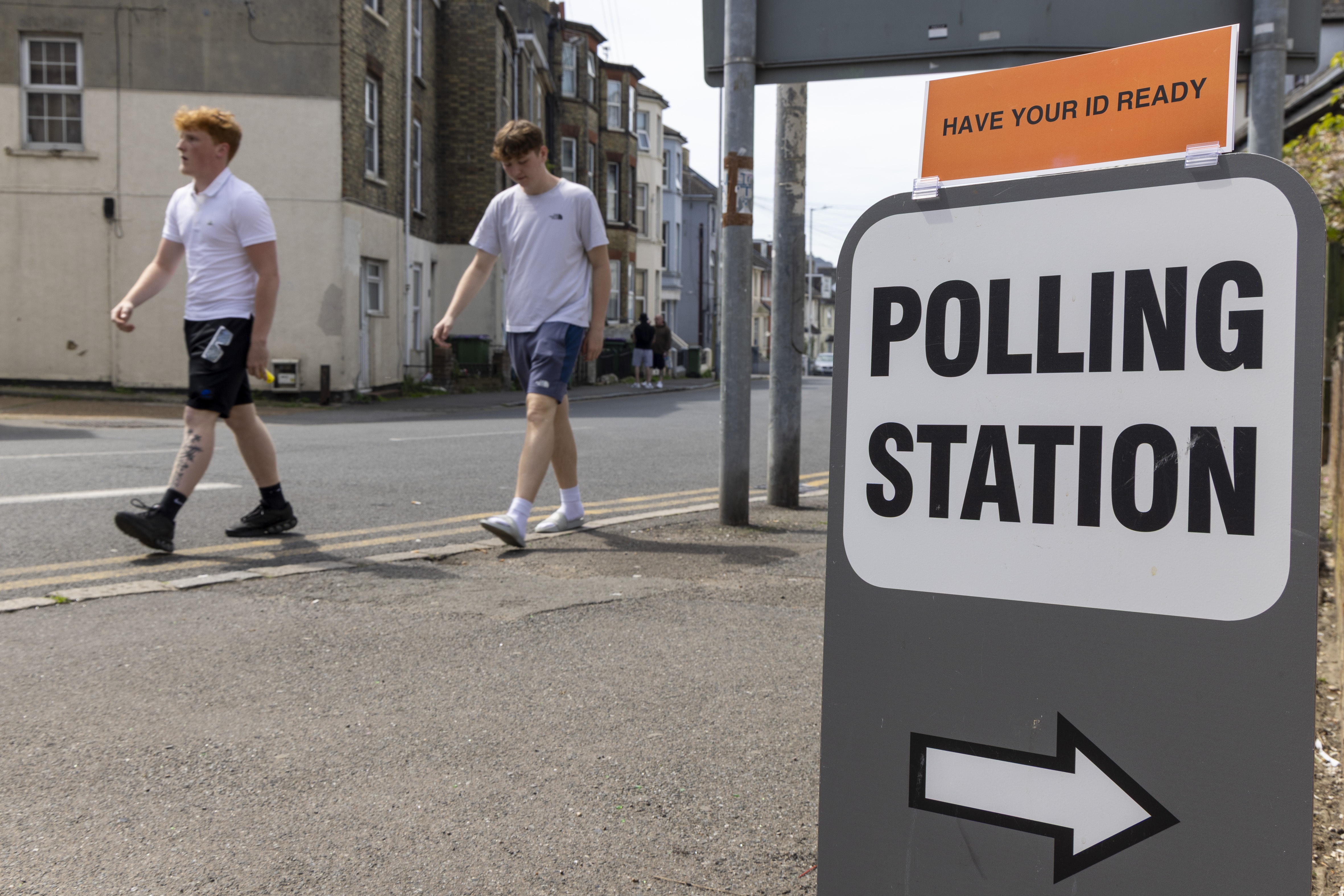 People walk past a sign for a polling station during local council elections in Folkestone, England in May. The British government is announcing plans to lower the voting age to 16.
