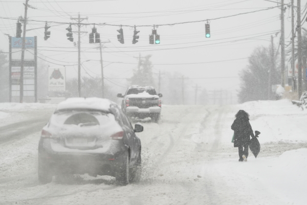 Heavy snow falls as cars drive by a person in a parka carrying a bag who is walking along U.S. Route 42 in Florence, Ky., on Monday.