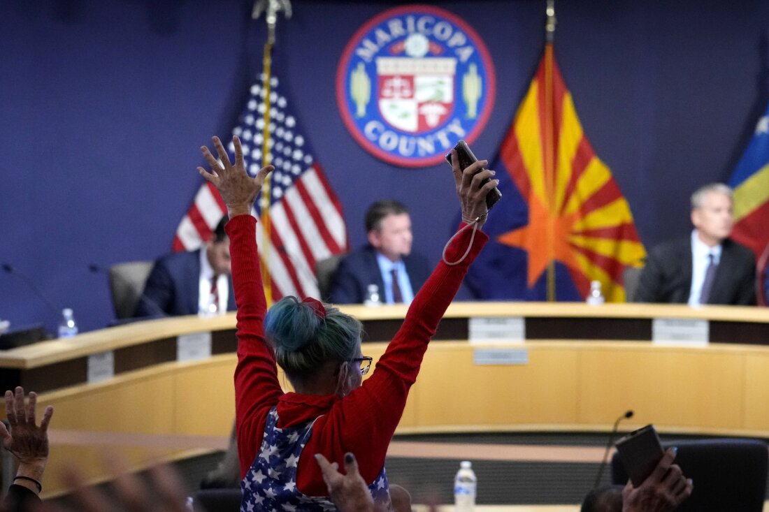 A woman stands in protest as the Maricopa County Board of Supervisors meets to discuss general election results on Nov. 28, 2022, in Phoenix.