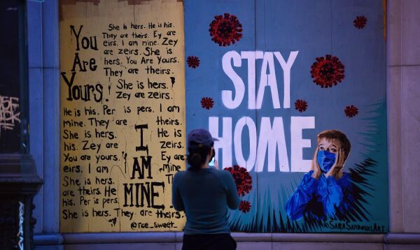 A woman stops to view a public art installation aimed at turning boarded up shopfronts into works of art. It says "stay home."