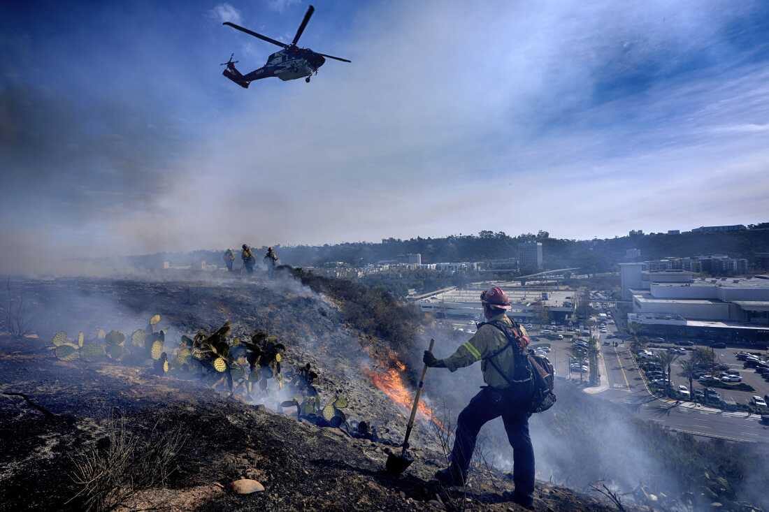 San Diego firefighters knock down a small brush along a hillside over the Mission Valley Shopping Mall in San Diego on Tuesday.