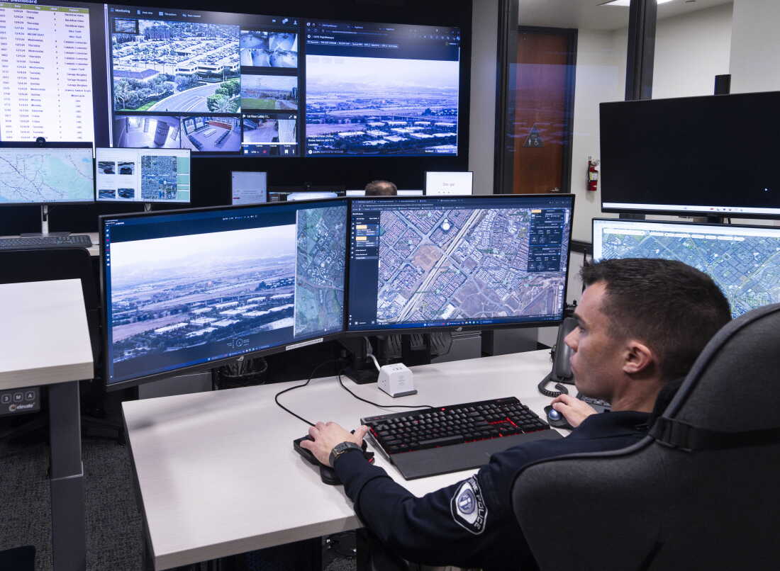 A police officer sits at a desk with multiple computer screens as he monitors video surveillance in the real-time crime center at the Irvine Police Department in California in 2024.