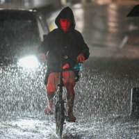 A man rides his bike along a flooded road near Chiba metro station in Chiba, Japan, on Aug. 13, 2026, as heavy rain swept through the area. Torrential rain pummeled eastern Japan, triggering landslides and power outages, and prompting the weather authority to issue its highest-level heavy rain warning for the region for the first time.