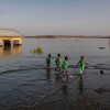 Okul çocukları, Kenya'nın Komote kentindeki El Molo Bay ilkokulunda su altında kalan ve terk edilmiş okul binalarının yanından sığ sularda yürüyor. Okuldaki öğretmenler, binaların timsahların üreme alanı haline geldiğini söylüyor.