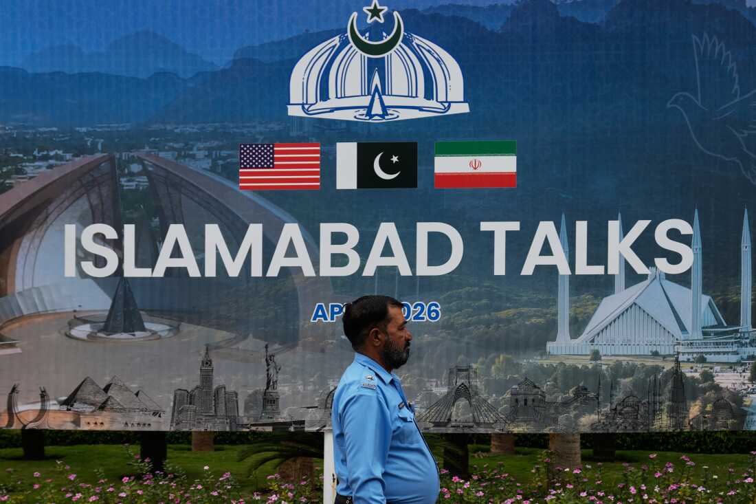 A police officer walks past a billboard regarding the United States and Iran negotiations, outside a media facilitation center in Islamabad, Pakistan, Saturday, April 11, 2026.