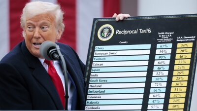 President Trump holds up a large board displaying a list of tariff rates on imports from a list of countries, on April 2, 2025. He's standing outdoors in the White House's Rose Garden and is speaking into a microphone that's attached to a lectern.