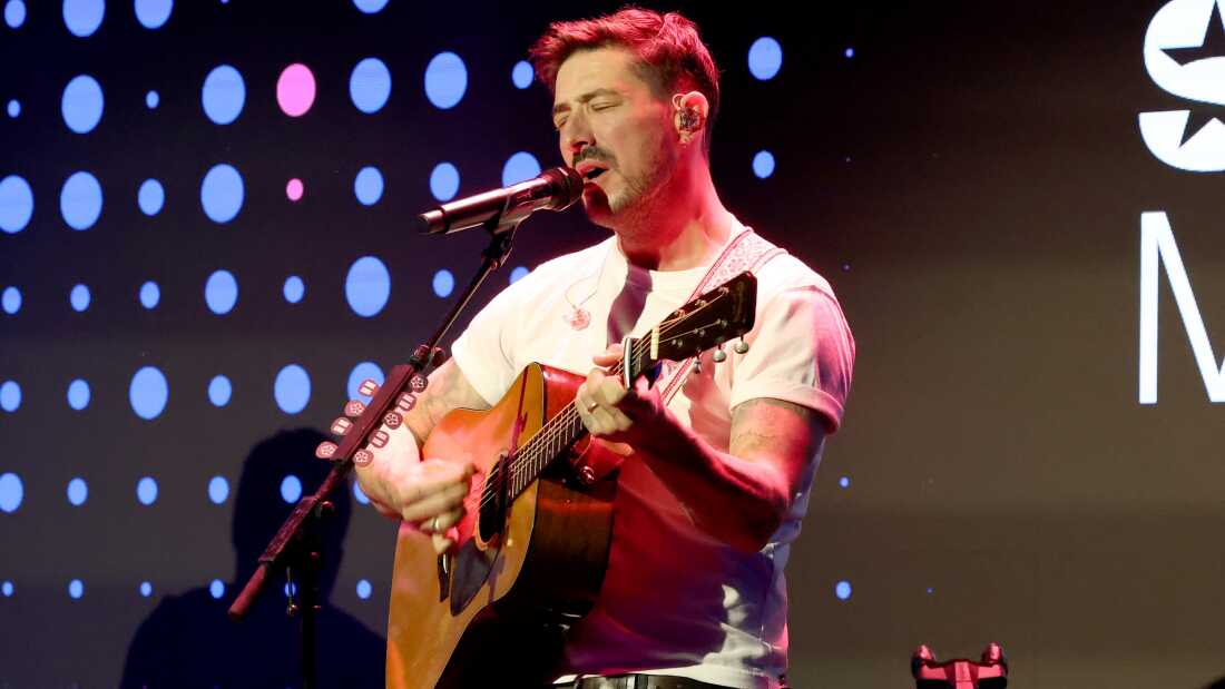 马库斯·芒福德闭着眼睛,对着麦克风唱歌,弹着吉他。