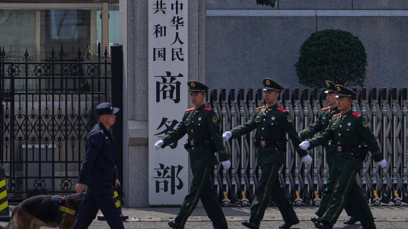 FILE - Paramilitary soldiers and a police officer with a sniffer dog march past the main entrance gate of China's Ministry of Commerce, in Beijing, on April 3, 2025.