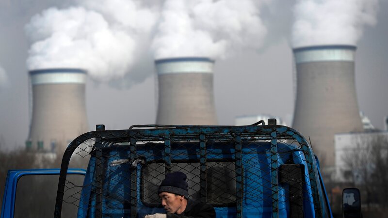 FILE - A worker throws his cigarette on a truck parked in front of a cooling towers of a coal-fired power plant in Dadong, Shanxi province, China, on Dec. 3, 2009. 