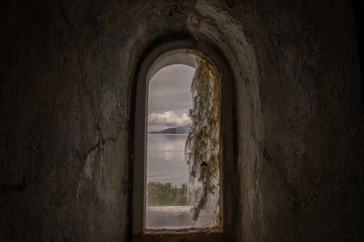 A window view from inside the San Isidro Lighthouse, which is located at the southern tip of the Brunswick Peninsula, in the region of Magallanes and Chilean Antarctica in Chile, with the Darwin Mountain Range in the background.