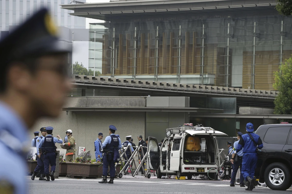 Police officers work near a vehicle, center, which was stuck against a barricade near the prime minister's office, background, in Tokyo on Saturday.