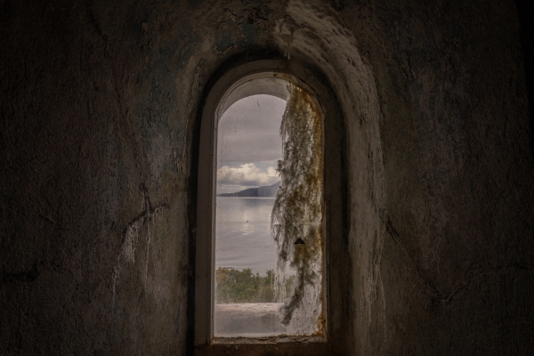 Window view from inside the San Isidro Lighthouse, which is located at the southern tip of the Brunswick Peninsula in the XII Region of Magallanes and Chilean Antarctica in Chile, with the Darwin Mountain Range in the background and next to a dense native forest.Patagonia, Chile, on Tuesday, November 5, 2024. Tamara Merino for NPR.