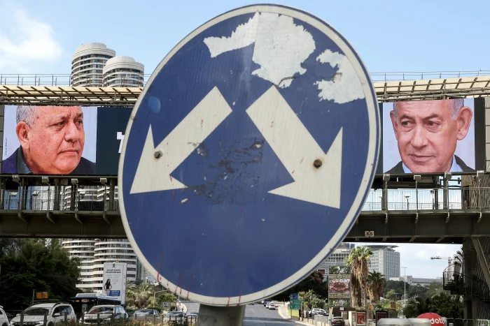 A road sign stands in front of a large billboard featuring Israel