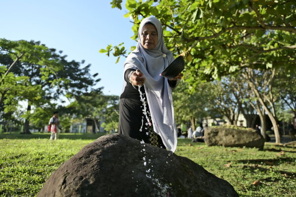 A woman sprinkles water on a stone marking a mass grave of victims of the 2004 Indian Ocean tsunami in Banda Aceh, Indonesia, Thursday, Dec. 26, 2024.