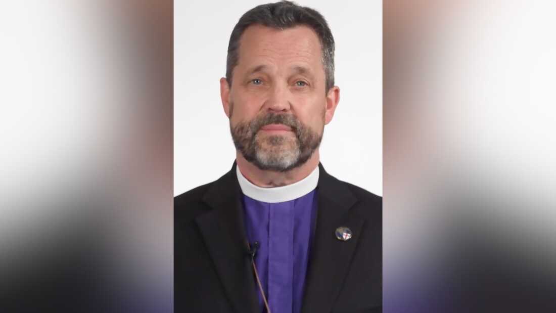 A screenshot of Archbishop Steve Wood wearing a blue shirt, white clerical collar and black blazer.