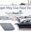 Cars with people inside are lined up at a food distribution event in Houston in November 2025. In the background is a large truck that says on its side: "Hunger May Live Next Door."