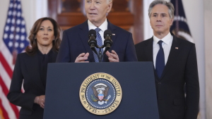 Joe Biden speaks at a White House podium, with Kamala Harris standing behind him at left and Antony Blinken at right.