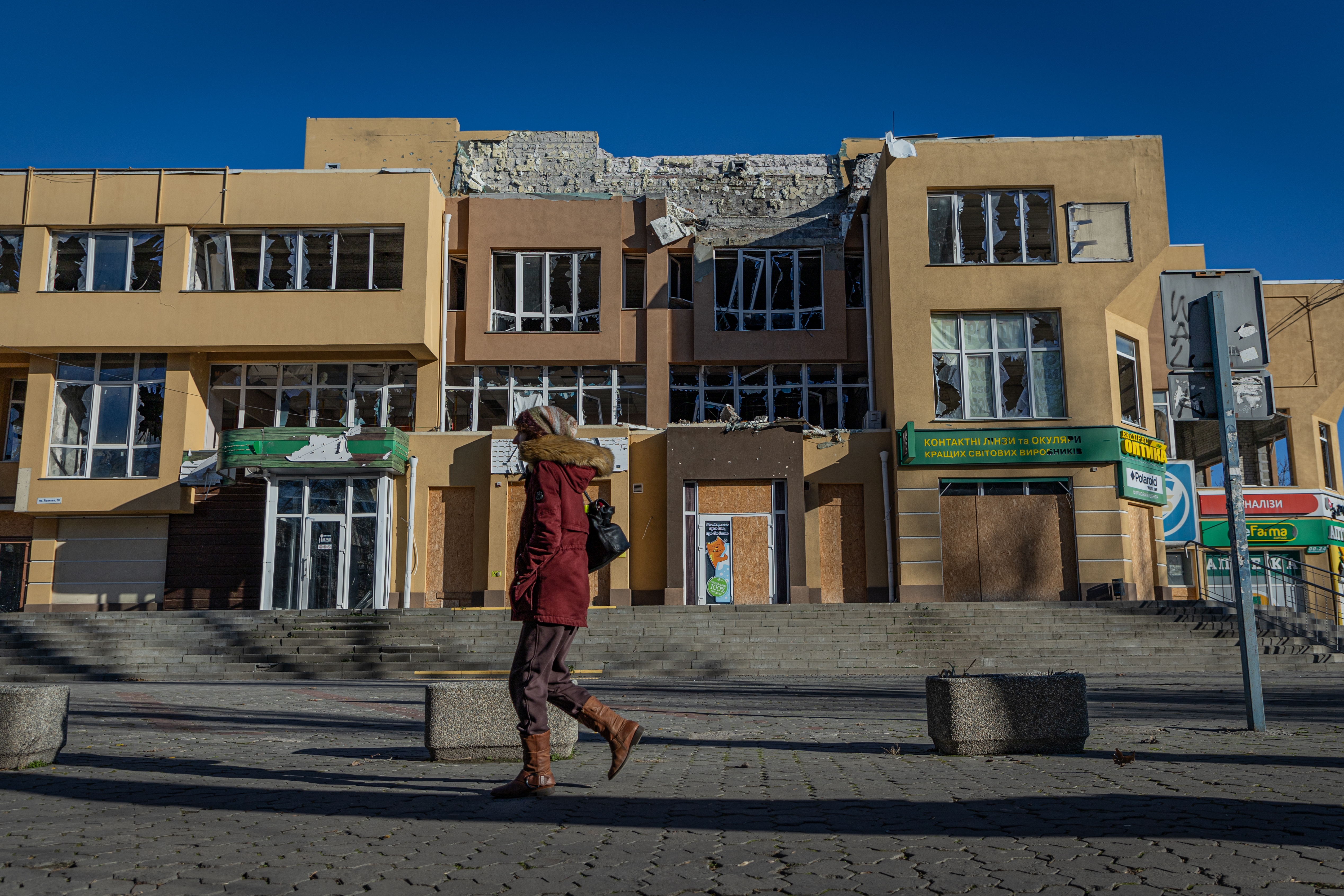 A woman walks in front of a war-ravaged shopping complex in Kherson, Ukraine, on Jan. 4. People in the city say cloudless days are most dangerous because Russian drones take advantage of the high visibility to swarm over the front-line city.