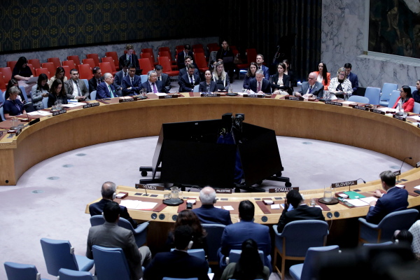 Members of the United Nations Security Council sit around a large horseshoe-shaped desk as they vote on a resolution.