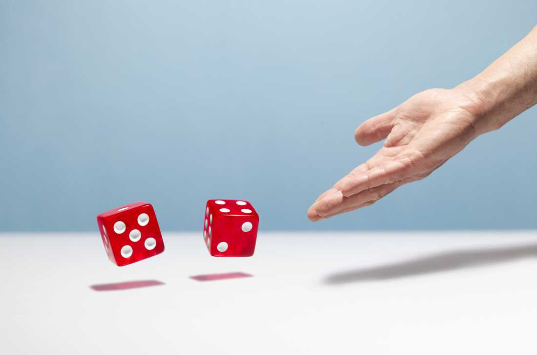 A man's hand is shown throwing a pair of red dice.