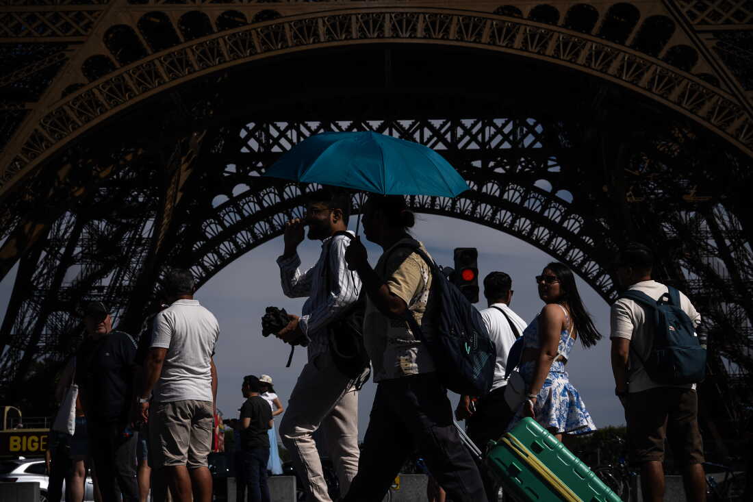 FILE - People walk with an umbrella near the Eiffel Tower in Paris during a heat wave July 11, 2026.