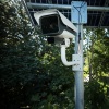A car drives past an automatic license plate reader that has a camera mounted on a pole to monitor traffic.