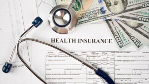 A stethoscope, calculator and $100 bills are shown with a form that says "Health Insurance."