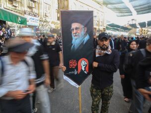 A man carries a large banner featuring a portrait of Iran's slain Supreme Leader Ali Khamenei amid crowds of pilgrims on a street in Karbala during Arbaeen.