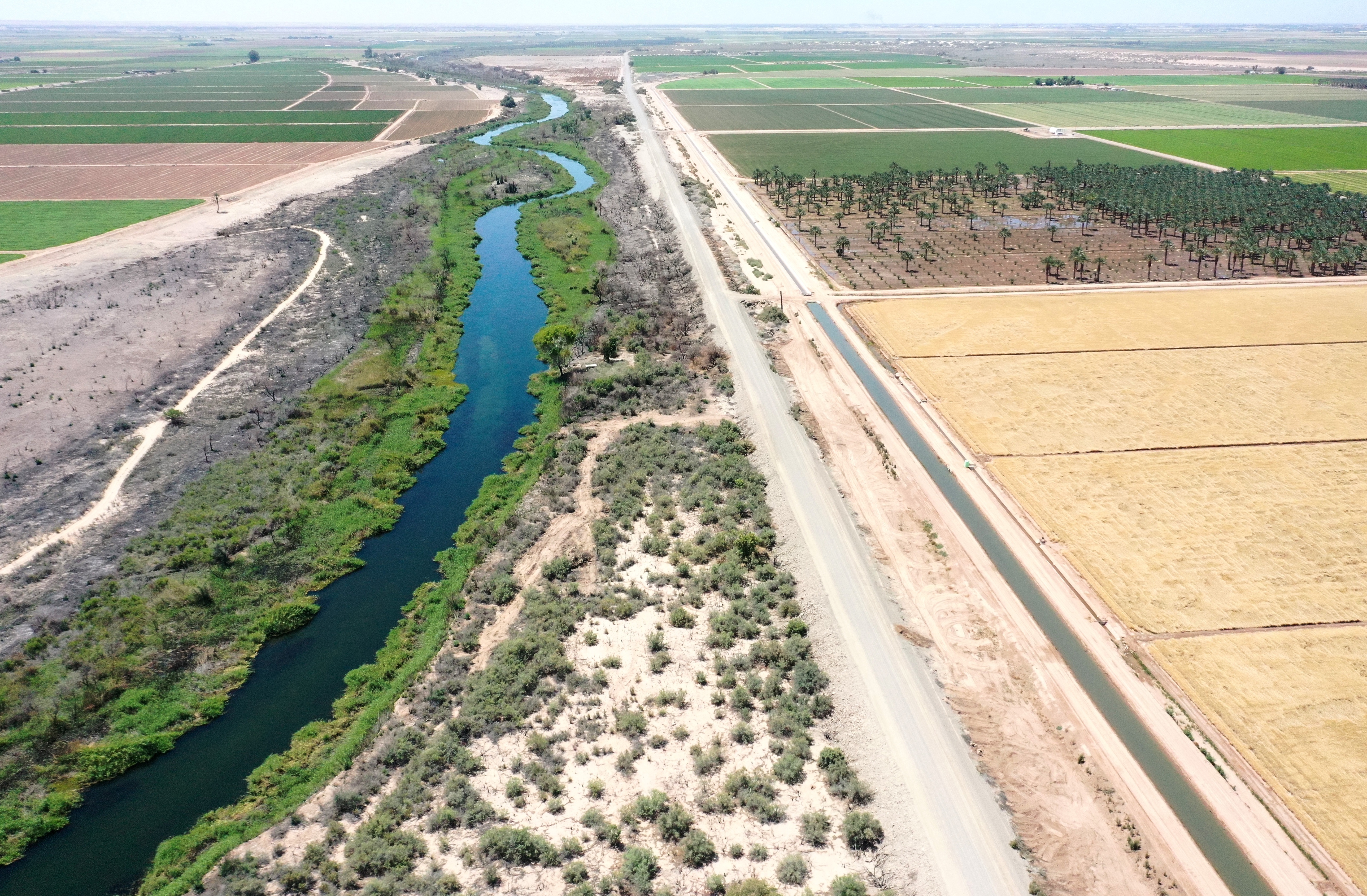 An aerial view shows the long-depleted Colorado River (L) as it flows between California (R) and Arizona, and an irrigation ditch (R) carrying river water toward Quechan tribal land on May 26, 2023 near Winterhaven, Calif.