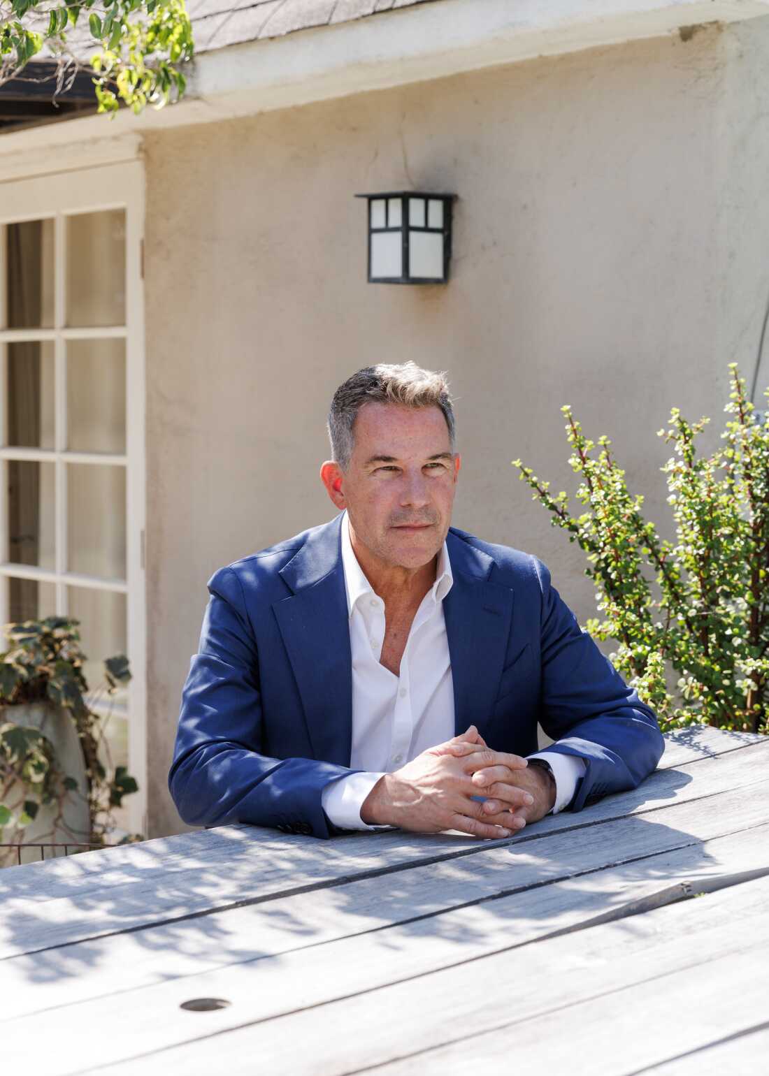 This photo shows Jeremy Bernard seated outdoors at a wooden table. He's wearing a blue suit jacket and a white shirt. This photo shows Jeremy Bernard seated outdoors at a wooden table. He's wearing a blue suit jacket and a white shirt.