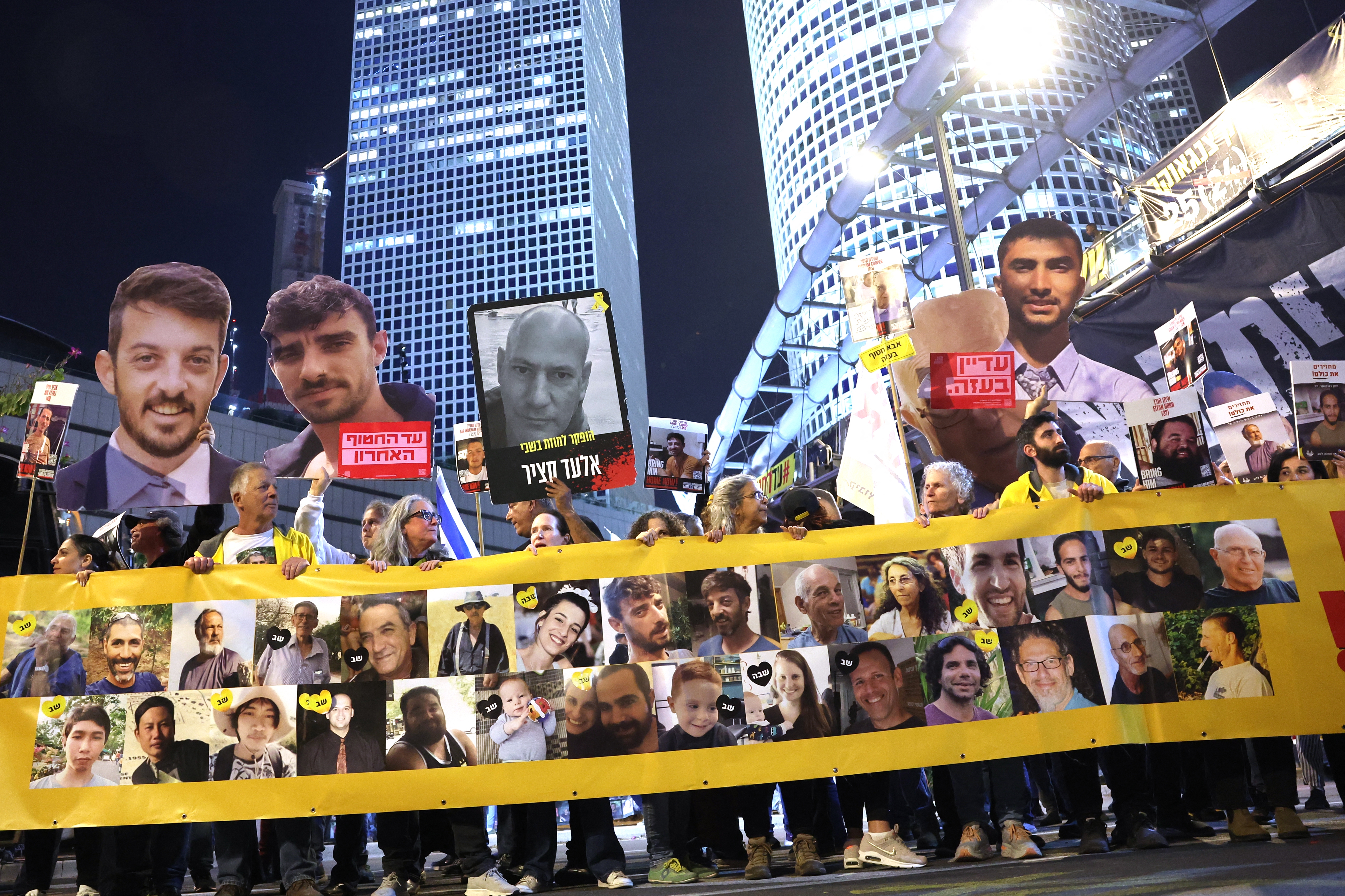 Friends and relatives of Israeli hostages held captive since the October 7, 2023 attacks by Palestinian militants in the Gaza Strip, stand behind a banner bearing their portraits during a demonstration calling for action to secure their release in front of the Israeli Defense Ministry in Tel Aviv on Tuesday.