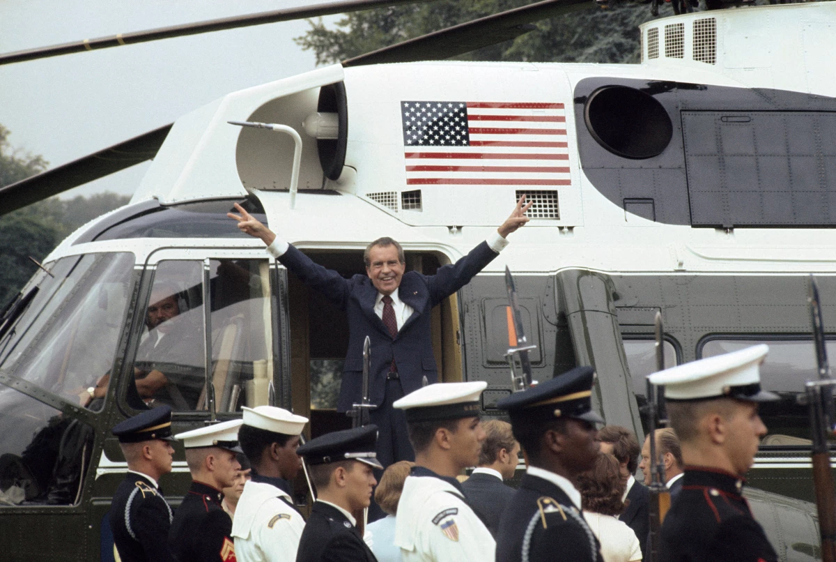 As he boards the White House helicopter after resigning the presidency, Richard Nixon smiles and gives the victory sign.