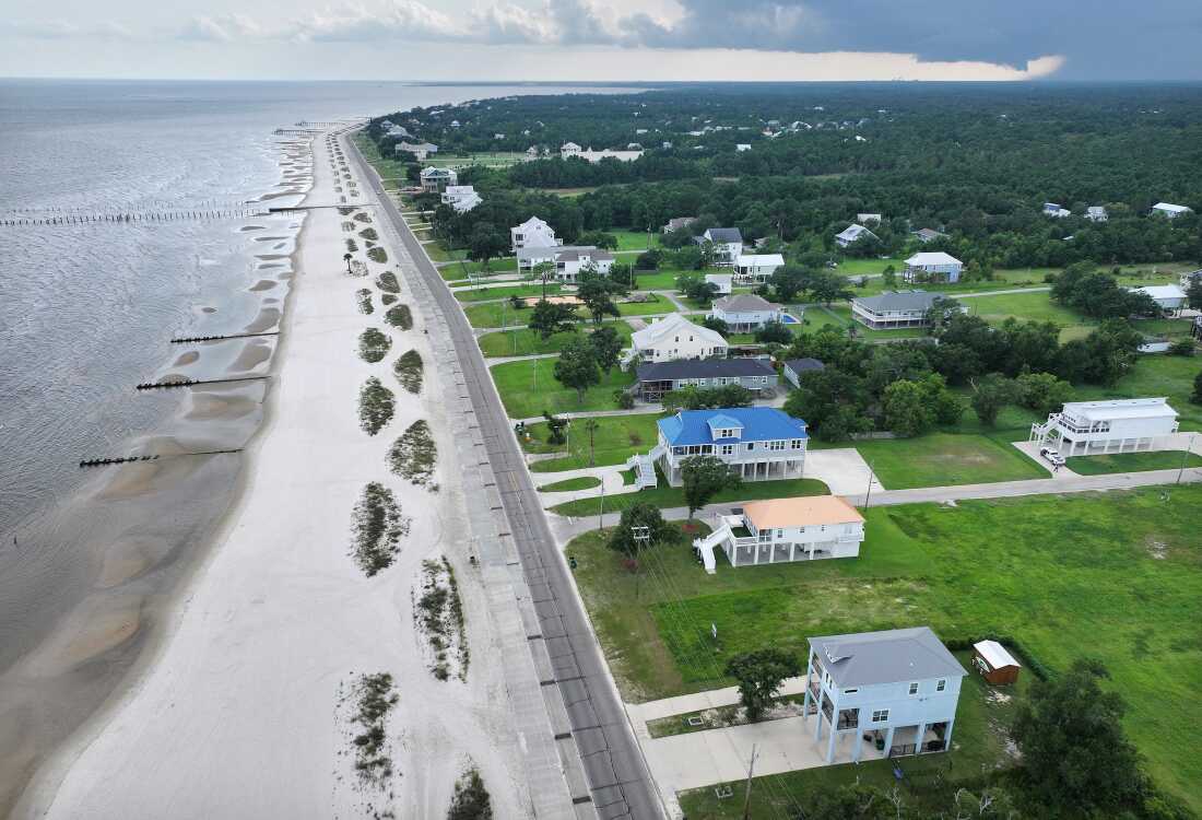 An aerial view of rebuilt elevated homes with green lawns along the sandy Waveland Beach in Mississippi, an area hard-hit by Hurricane Katrina 20 years ago.