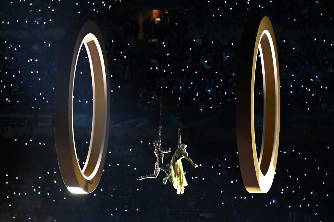 Two performers are suspended between two large rings.
