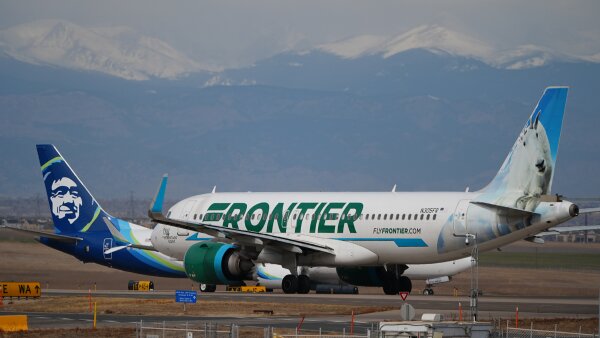 A Frontier Airlines jetliner waits for clearance to take off at Denver International Airport. Mountains are visible in the background. 