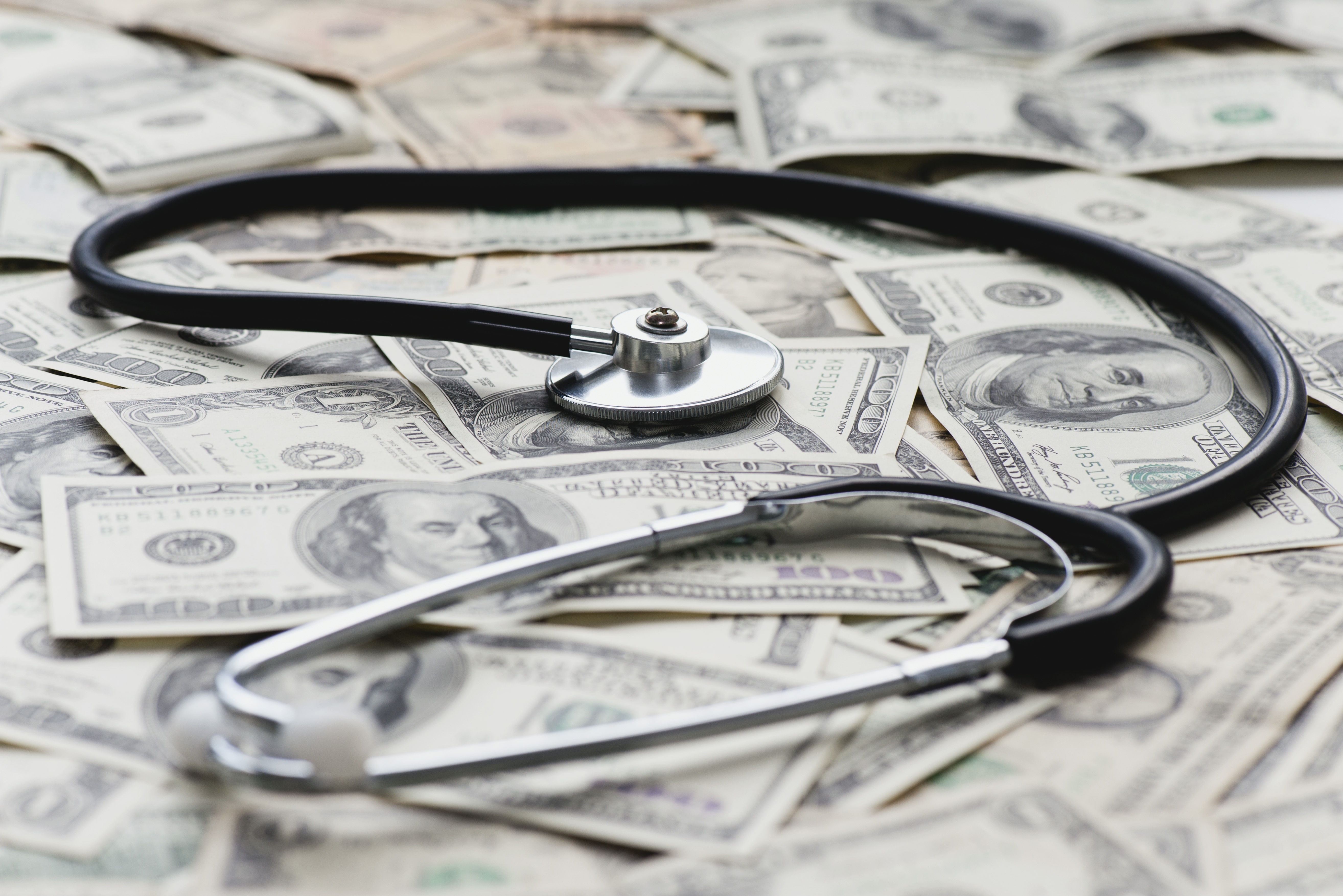 A stethoscope sits on a pile of U.S. bank notes. (Odilon Dimier via Getty Images)