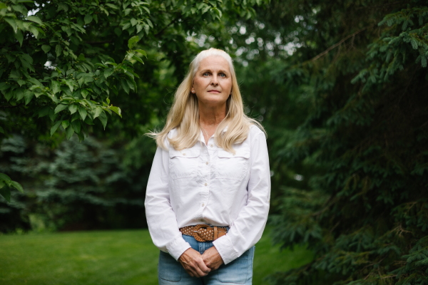 Rebecca Norton is shown standing alone outside with lush green trees around her.