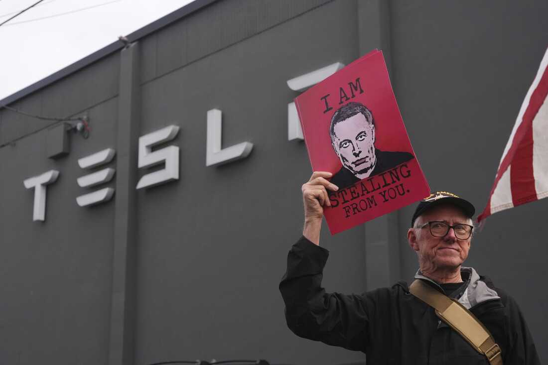A man holds a sign with Elon Musk's face and the slogan "I am stealing from you" on it during a protest against Musk and Tesla on Saturday in Seattle.