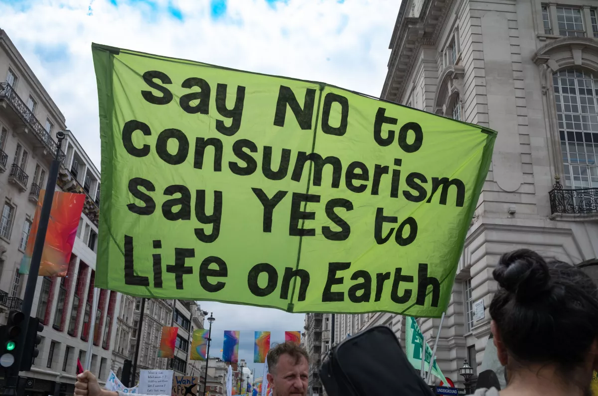 At a rally in 2024, climate activists carry a banner opposing consumerism. Advocates for population decrease believe fewer humans could mean less consumption, a drop in carbon pollution and a restoration of wild habitats.