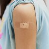 A girl's T-shirt sleeve is rolled up, revealing a bandage after receiving a vaccine in the upper arm.