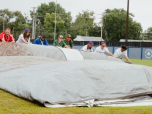 Players with the Boston Hunters and the San Francisco Firebells assist the grounds crew in rolling up the infield tarp prior to the start of the WPBL's inaugural game on Saturday, Aug. 1.