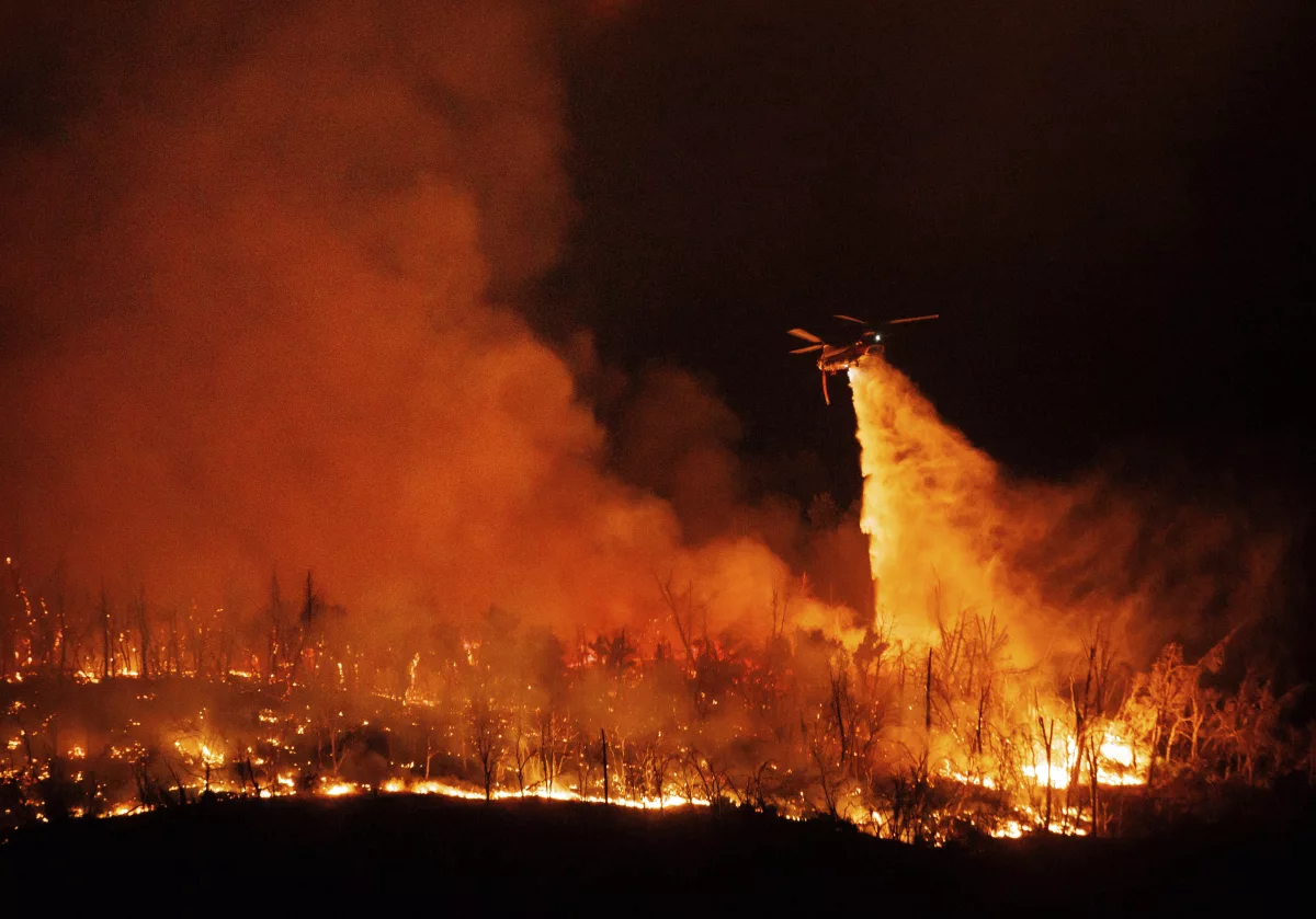 A night flying helicopter drops water on flames as the Thompson Fire burns Tuesday in Oroville, Calif.