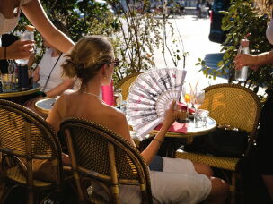A young woman sitting on a terrace shields herself from the sun with a fan decorated with Parisian landmarks during a severe heat wave in Paris on Aug. 12, 2026.