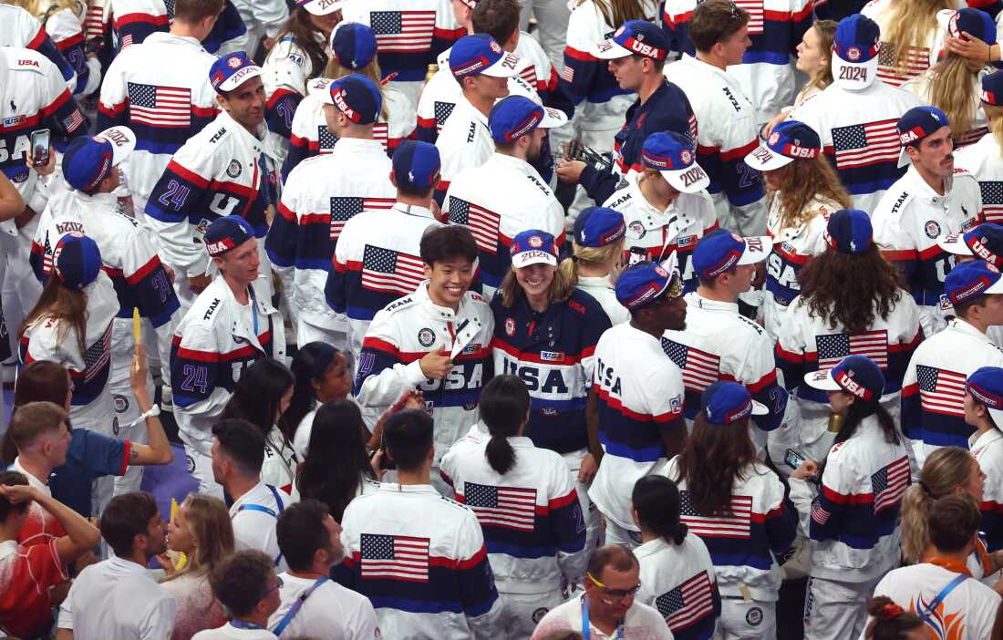 オリンピック閉会式で、大勢の米国選手が集まる中、旗手を務めるケイティ・レデッキー選手が他の米国選手とともにポーズをとっている。
