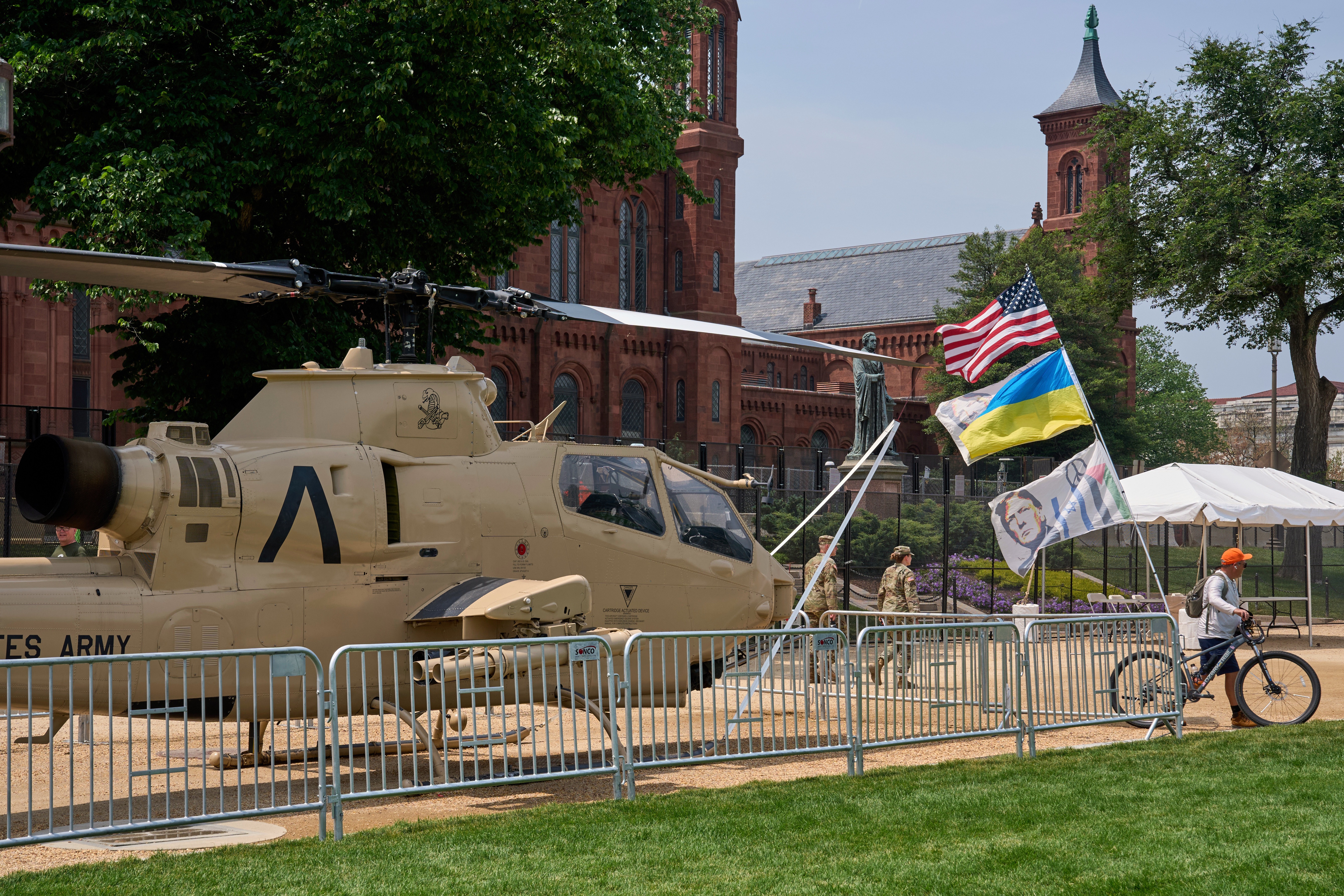 A man bicycles with several flags past a helicopter on display during preparations for an upcoming military parade commemorating the Army