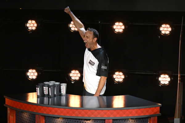 Joey Chestnut lifts his fist in excitement onstage, in his Unfinished Beef jersey.