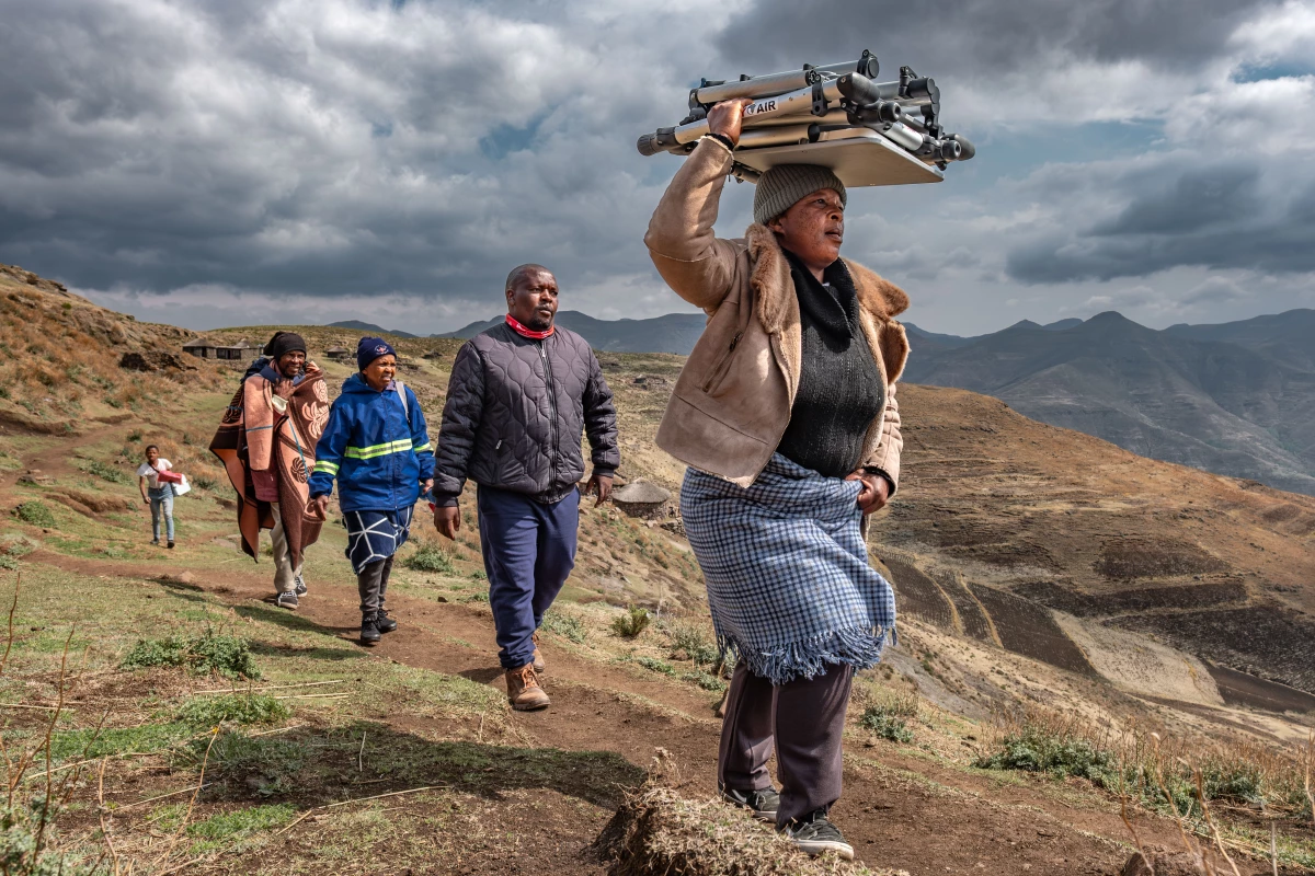Villagers from Mphooko helps members of the Lesotho Flying Doctor Service carry their equipment after being dropped off by helicopter on the nearest stretch of flat land.